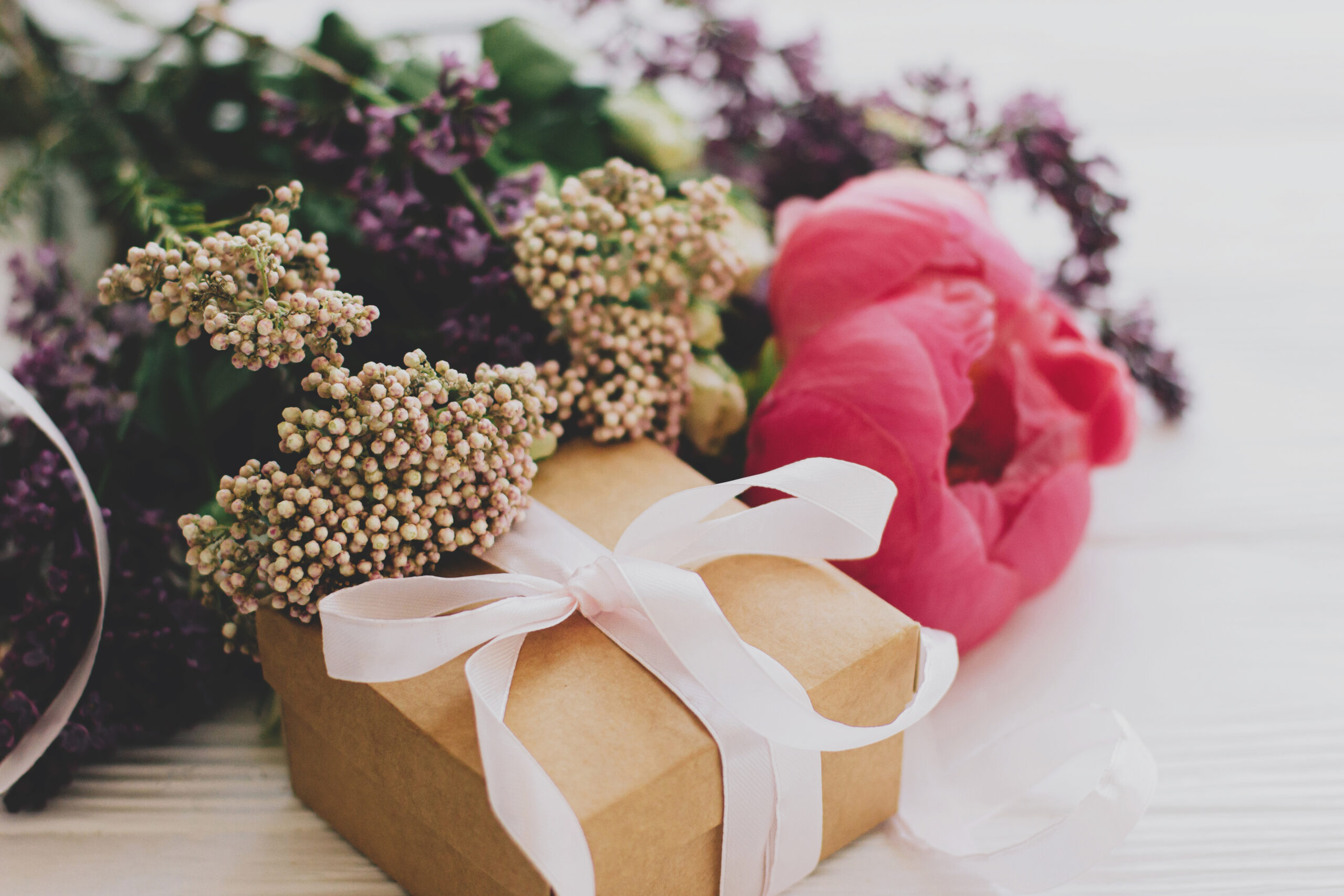 Happy mothers day and valentines day concept. Stylish craft gift box and bouquet with peony, lilac and roses flowers on white wooden background close up